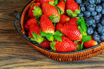 Healthy berries and strawberries in a basket wooden background