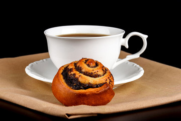 A cup of coffee a bun with poppy seeds on a black background
