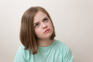 Naklejka premium Indoor portrait of beautiful girl with bob hairstyle in blue green t-shirt looking pensive and thoughtful as if thinking, dreaming or remembering, frowning a bit. White background
