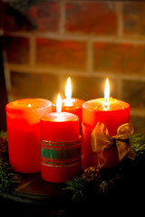 Four red candles with christmas decoration in atmospheric light. Moody. Authentic.