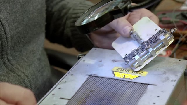 Engineer preparing new chip processor for installation on motherboard of smartphone iphone. White man in old workshop