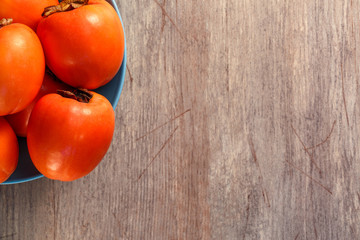 Ripe persimmons in plate on the table, top view