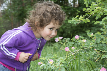 Naklejka na ściany i meble Spring in the forest a little curly-haired girl sniffs a flower