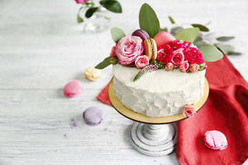 Delicious creamy cake with flowers and macaroons on wooden table closeup