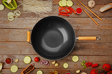 Empty wok pan with fresh ingredients and spices on wooden background, top view