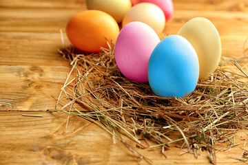 Decorative nest with colourful Easter eggs on wooden background