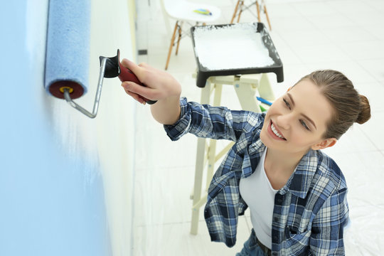 Beautiful young woman painting wall in room