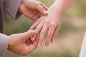 Closeup of a groom putting a gold wedding ring onto the bride's finger