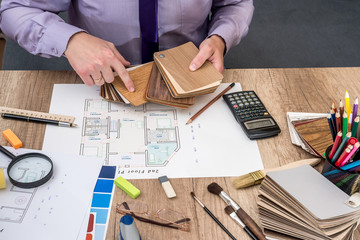 Man architect draws a house plan with color palette for  furniture, work tools.