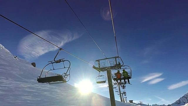 Two men are going up by chair ski lift on sunny day, Tignes, France