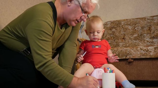 Attractive baby sitting on the pot and drawing with her grandfather markers on paper. The boy peeing and playing with the family home. Kid 1 year.