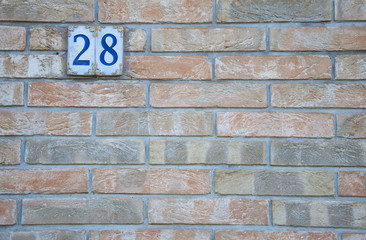 Fototapeta na wymiar Traditional Italian home sign board painted on ceramic tile placed on orange wall, with number 28.