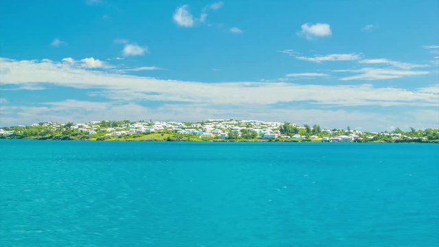 Sailing Past a Tropical Island in Bermuda, Featuring Turquoise Water and a Lush Green Island with Bermudian Architecture on a Sunny Day with White Clouds in a Blue Sky