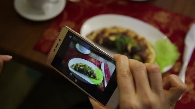 Trendy woman in a restaurant make photo of food with mobile phone camera for social network