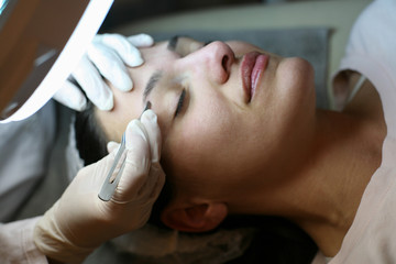 Young woman having eye-brows plucked. lying on the table.