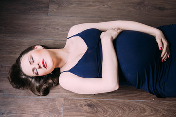 Fototapeta na wymiar Pregnant woman in dark blue dress lies on the floor with closed eyes