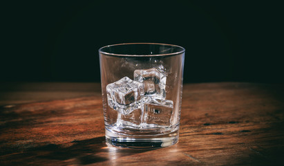 Glass with ice cubes on wooden counter