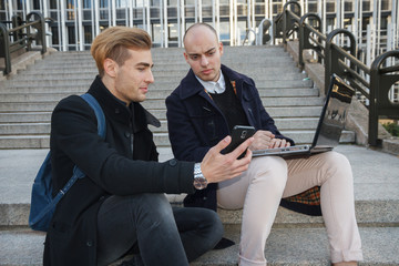 Two young entrepreneurs, one bald and the other with blond hair working with a laptop and the smart...