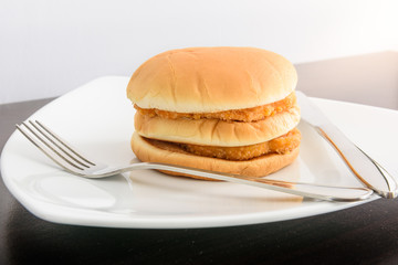 chicken hamburger in white plate with knife and fork, on top tab