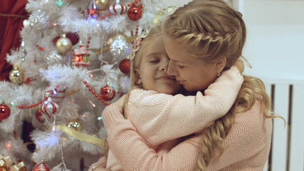 Mother and daughter hug and kiss each other near a Christmas tree