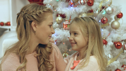Obraz na płótnie Canvas Daughter hugging and kissing her mother near Christmas tree