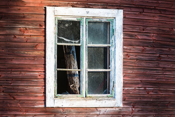 Broken window on an old red wooden house. Wooden debris inside.