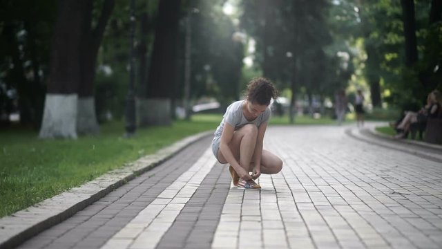 Girl in sneakers run in park and tyes shoelaces