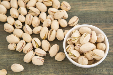 White bowl of pistachios on wooden background