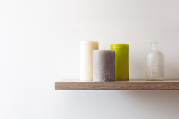 three candles and a bottle on a wooden shelf
