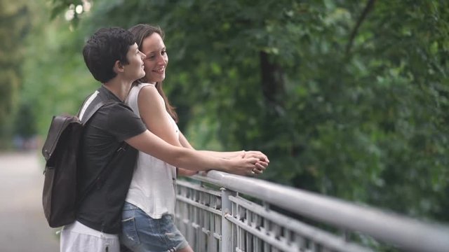 Two young girls hugs, kisses and talk on a bridge