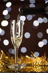 Bottiglia che versa in bicchiere flute vino spumante, con luci di sfondo e decorazioni festive