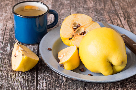  Guince.    Blue metal plate with fresh fruits of quince, whole and cut into slices, and a mug with compote on old wooden table.