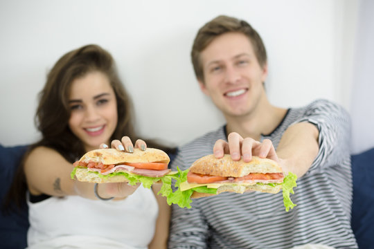 Closeup picture of hamburgers represented by young couple lying in bed at home. People prefer having morning breakfast all together.