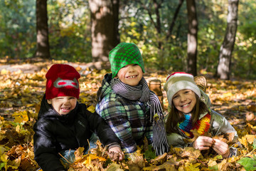 Older sister and two younger brothers in autumn leaves Happy