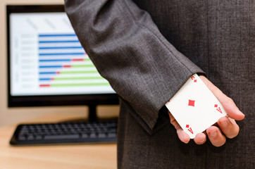 Businessman holding an ace card in his hands, hidden behind him, with desktop and a computer on the...