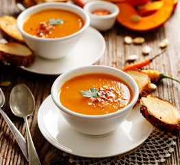 Homemade pumpkin soup in a white ceramic bowl on a wooden rustic table, nutritious and delicious vegetarian dish