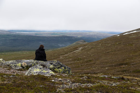 Man in black jacket sits on rock looking at mountains
