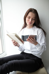 Young woman sitting with notebook and smartphone on windowsill