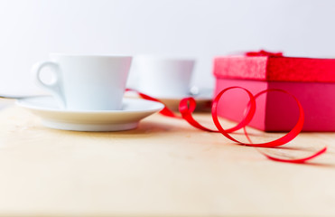 Cups with coffee, gift box, decorated by ribbon on wooden table.