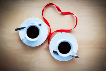 Cups with coffee, decorated by ribbon on wooden table.