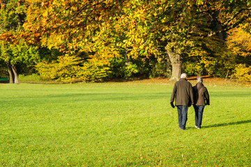 Coppia di anziani a passeggio in autunno all'Englischer Garten di Monaco di Baviera, Germania