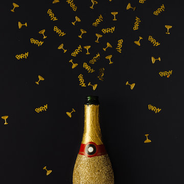 Golden champagne party bottle with confetti on dark background.