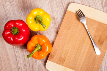 Three colors the peppers on wood cutting background with fork. Yellow, orange and red peppers. Popular pepper in kitchen.