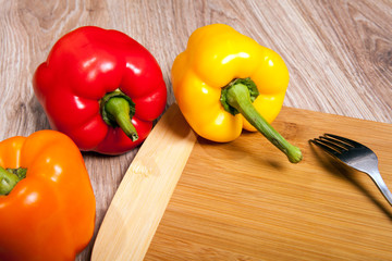 Three colors the peppers on wood cutting background with fork. Yellow, orange and red peppers. Popular pepper in kitchen.