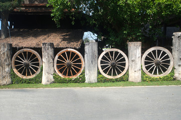 Fototapeta na wymiar An old wheel of a traditional cart leaning on a wooden fence.