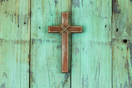 Rugged wood cross hanging on rustic mint green painted background