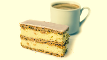 Sweet cake. Puff cake with cream. Cup with black coffee in the background. Selective focus. Isolated objects.