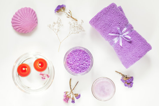 Spa products. Lavender bath salts, dry flowers, soap, cosmetic cream, light candles and towel. Violet purple concept. Flat lay on white background, top view.