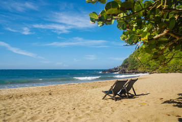Two chairs in the shore of a beach in a sunny day.