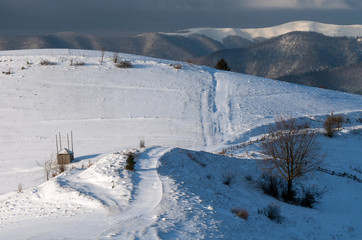 Fototapeta premium Covered in snow country road in the hills on the background of mountain ridge. Winter landscape.
